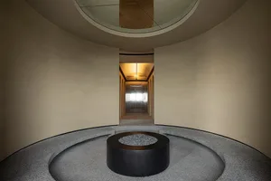 Modern lobby with a circular concrete floor, glass walls, and a central fire pit.