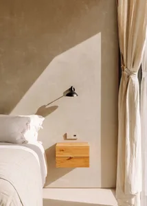 Minimalist bedroom with a wooden floating nightstand, window with curtains, and soft lighting from a wall-mounted sconce.