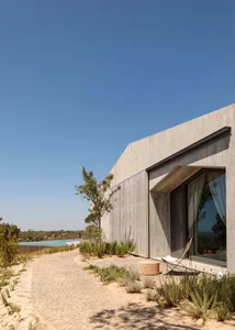 A modern minimalist house featuring concrete and glass exteriors surrounded by natural surroundings.