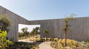 A minimalist residential exterior with a concrete wall and natural landscape.