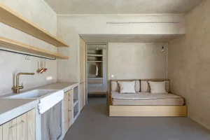 A minimalist residential kitchen featuring a concrete countertop and floor, with a modern sink and open shelving.