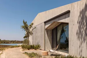 Modern house with concrete exterior and large window overlooking a pool and landscape.