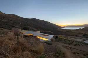 A modern, minimalist vacation home with concrete and glass features on a desert hillside.
