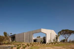 A modern residential building with a concrete exterior and a large arched opening on a clear, sunny day.