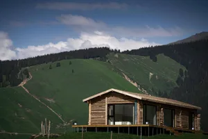 A cozy, rustic living room with wooden furniture and a large window overlooking green hills.