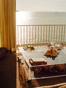 Glass table with books, a fruit bowl, and drink glasses, overlooking the ocean.