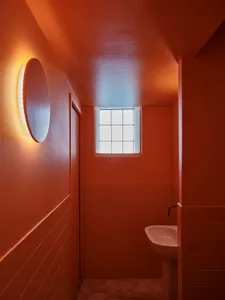 A minimalist bathroom with orange tiles, a window, and a sink.