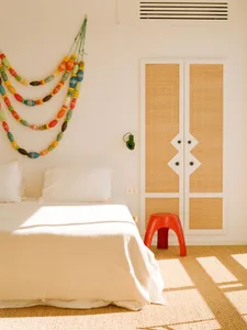 A minimalist bedroom with a bed covered in a white sheet and pillows, adorned with a colorful beaded garland hanging on the w