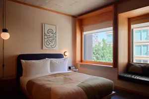 A minimalist bedroom with a wooden bed frame, white bedding, and a wall-mounted light fixture.