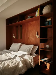 A minimalist bedroom featuring a wooden bookshelf with built-in lighting and storage.