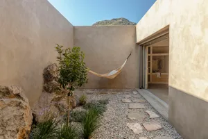 A minimalist residential garden with rock and slate features, including a hammock, small tree, and landscaping.