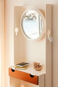 A minimalist wall-mounted desk with a round mirror above it, featuring a wood drawer and a decorative coral on the surface.