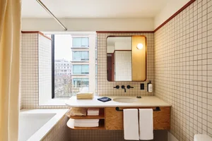 Modern bathroom with tiled walls and floor, white countertop, and a window.