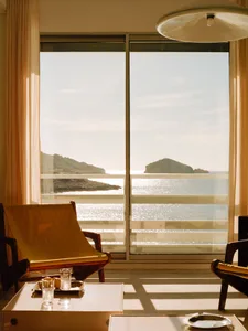 Modern living room with armchairs, coffee table, and a view of the sea through large windows.
