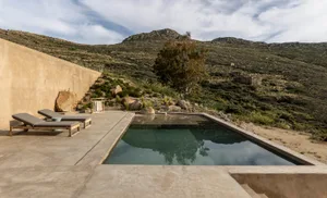 A modern outdoor living space featuring a sleek, rectangular pool with concrete surroundings, set against a backdrop of rocky