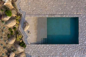 An aerial view of a modern pool with concrete, rock, and gravel elements.