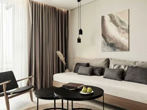 A modern residential living room featuring light-colored fabric seating, dark wood furniture, and minimalistic decor.