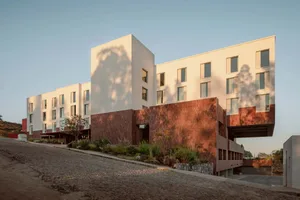 Modern residential building made of concrete, featuring large windows and a red brick wall.