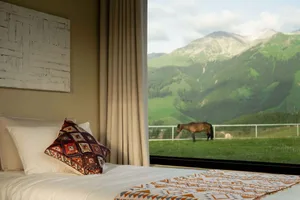 A bedroom with a bed featuring a bedspread and a pillow with a colorful geometric pattern, overlooking a mountain scene with 
