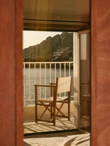 A wooden and canvas chair on a balcony overlooking a calm body of water and rugged mountains in the background.