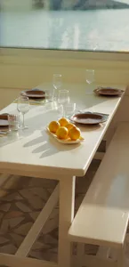 A white-painted wooden table with a plate of lemons and wine glasses set for dinner.