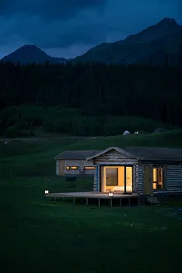 A cozy camping cabin with a wooden exterior and warm indoor lighting in a mountainous setting.