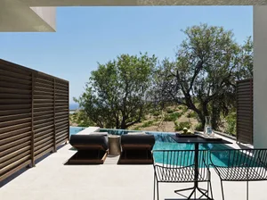 Modern, minimalist outdoor residential pool deck with concrete patio, lounge chairs, table, and infinity pool.