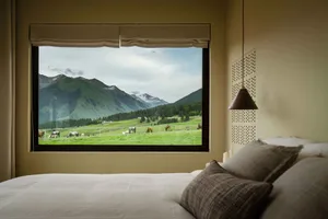 An interior design image of a modern bedroom featuring a large window with a scenic view of mountains and meadows, including 