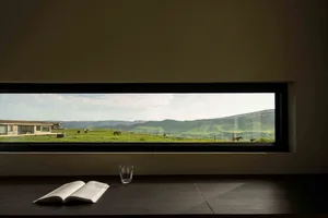 A modern window with a view of green mountains and a house in the background.