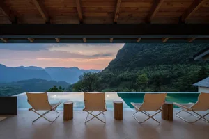A minimalist residential deck featuring concrete flooring, steel chairs, and wooden stools.