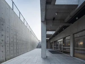 Modern commercial space featuring a minimalist design with concrete walls, a spacious walkway, and large glass doors.