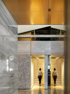 Two people walking up the stairs in a modern hotel lobby with marble walls and glass railings.