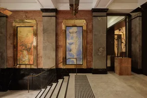 A modern lobby featuring marble walls and floors with a spiral staircase and framed artworks.