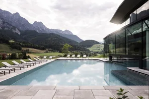 Modern outdoor swimming pool with lounge chairs and a mountainous landscape in the background.
