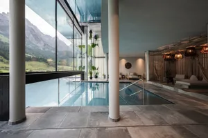 Modern pool lounge area with glass walls, concrete floor, and cushions.