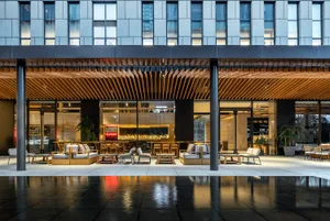 A modern restaurant interior featuring wooden tables and chairs, glass walls, and metal accents.