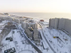 Aerial view of a snow-covered residential area with apartment buildings and a beach in the background.