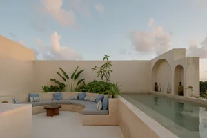 A minimalist residential patio featuring concrete seating areas, greenery, and a swimming pool under a clear sky with scatter