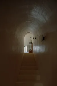 A modern staircase with smooth concrete steps, illuminated by overhead lighting, leading towards a light-filled space.