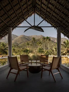 Outdoor seating area with woven bamboo furniture overlooking mountains and palm trees.