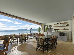 A cafe interior with wooden furniture, glass walls, and ceramic planters overlooking a bay.