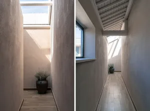 A minimalist corridor with wooden flooring and white walls, featuring a window at the end letting in natural light and a plan