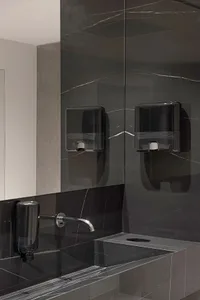 A modern bathroom featuring black marble walls and a white sink with a silver faucet.