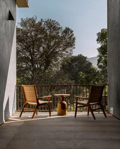 Two wooden armchairs and a wooden side table on a balcony overlooking forested mountains.