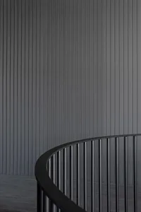 A modern minimalist staircase with a black metallic railing against a dark textured wall.