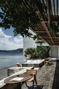 Modern outdoor space featuring stone-covered veranda with wooden furniture and greenery.