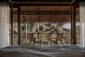 An inviting balcony featuring a wooden table and two woven chairs overlooking tropical foliage.