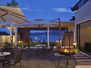 Outdoor patio area with metal furniture, leather accents, and cement flooring, featuring a fire pit and scenic lake view.