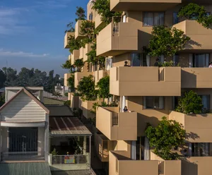 一座現代混凝土與玻璃立面的住宅建築，陽台與露台點綴綠意植物。