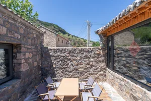 Outdoor dining area with stone walls and wooden furniture on a sunny day